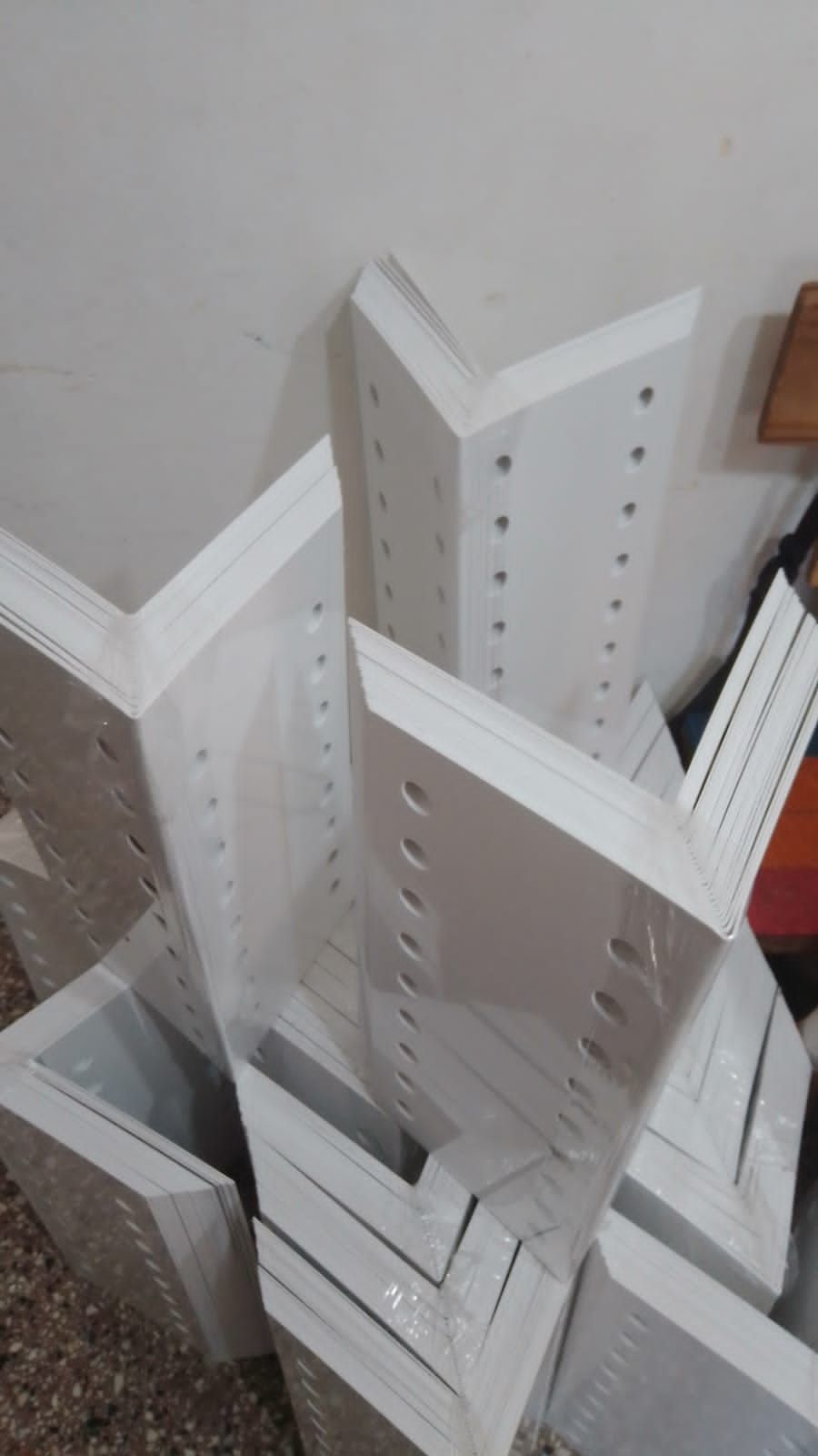 Soportes de esquina de metal blanco apilados contra una pared blanca.