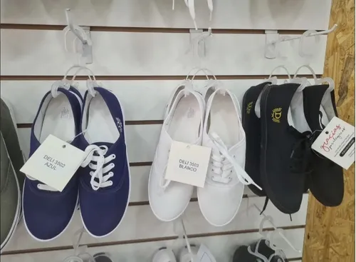 Zapatos expuestos a la venta en una pared. Zapatillas de lona azul marino, blancas y negras colgadas de los cordones.