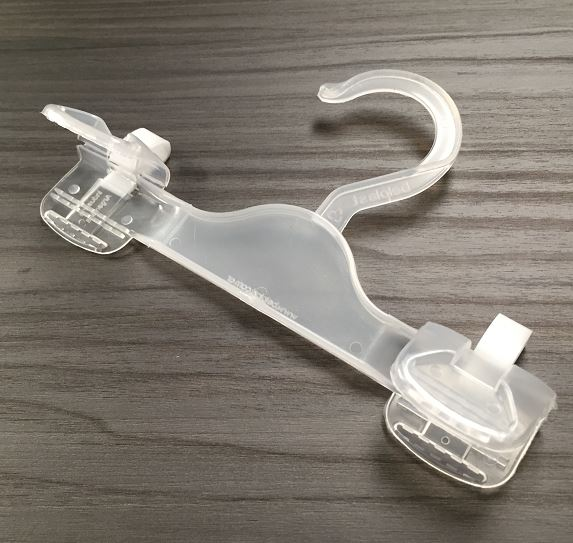 Percha para pantalones de plástico transparente con pinzas sobre superficie de madera.