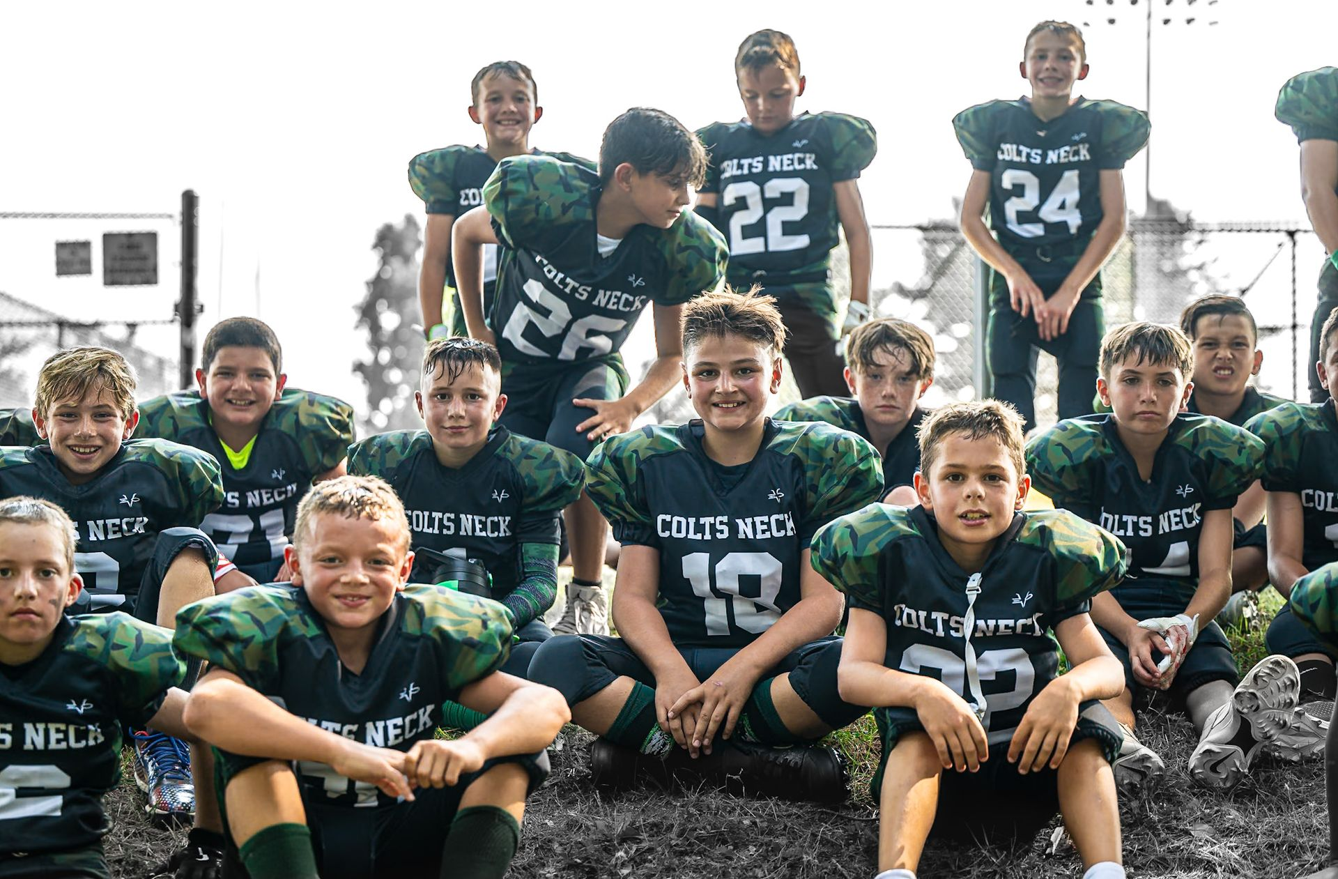 Football player in maroon jersey holding ball, smiling, surrounded by teammates on a field.