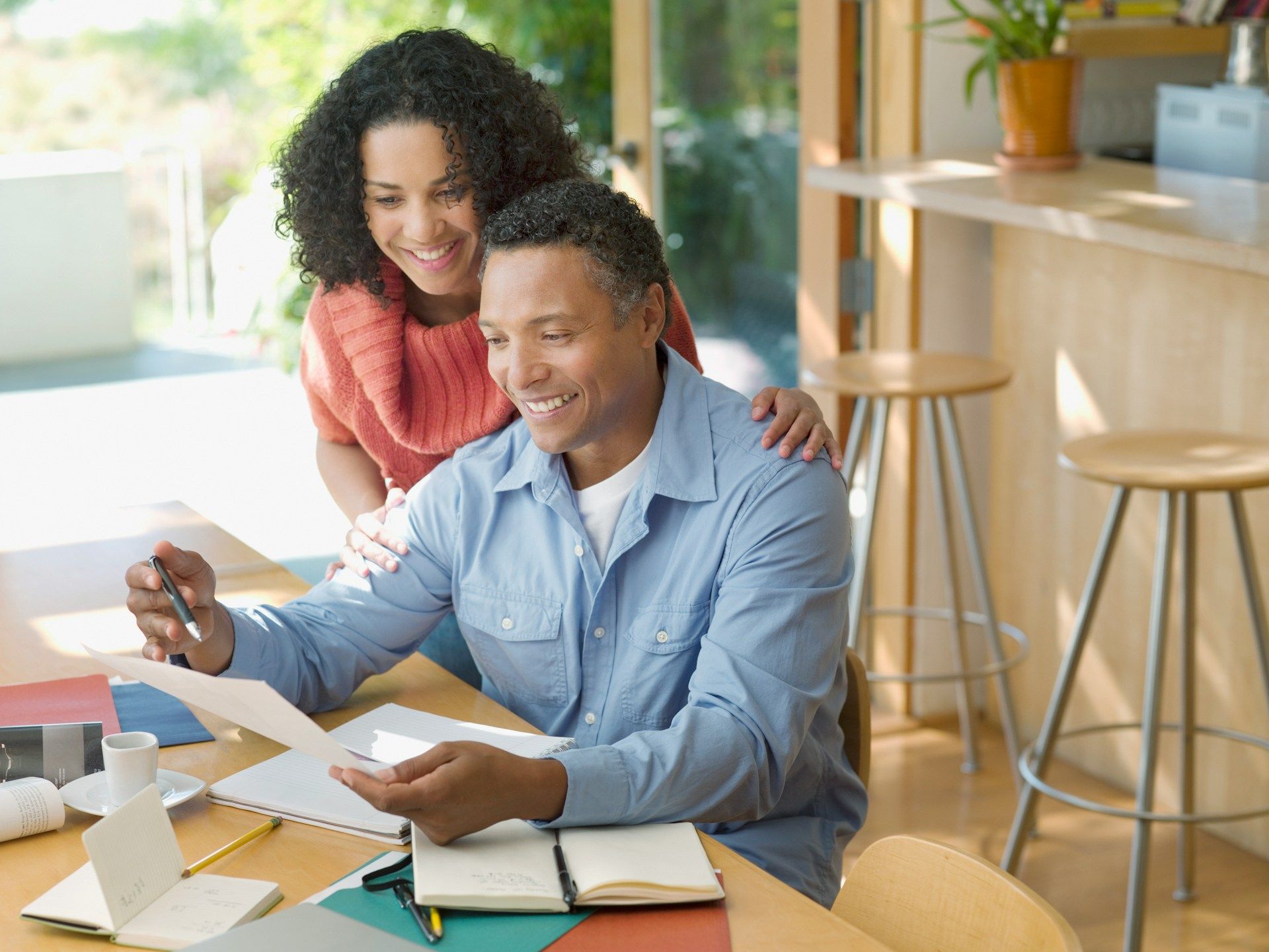 Two coworkers smiling at a desk, reviewing papers and using a laptop in a bright office