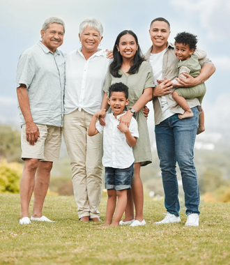 Family standing together outdoors on a grassy hill, smiling at the camera.