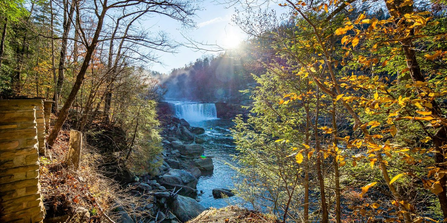 Sunlit waterfall flowing through a rocky forest gorge with autumn leaves