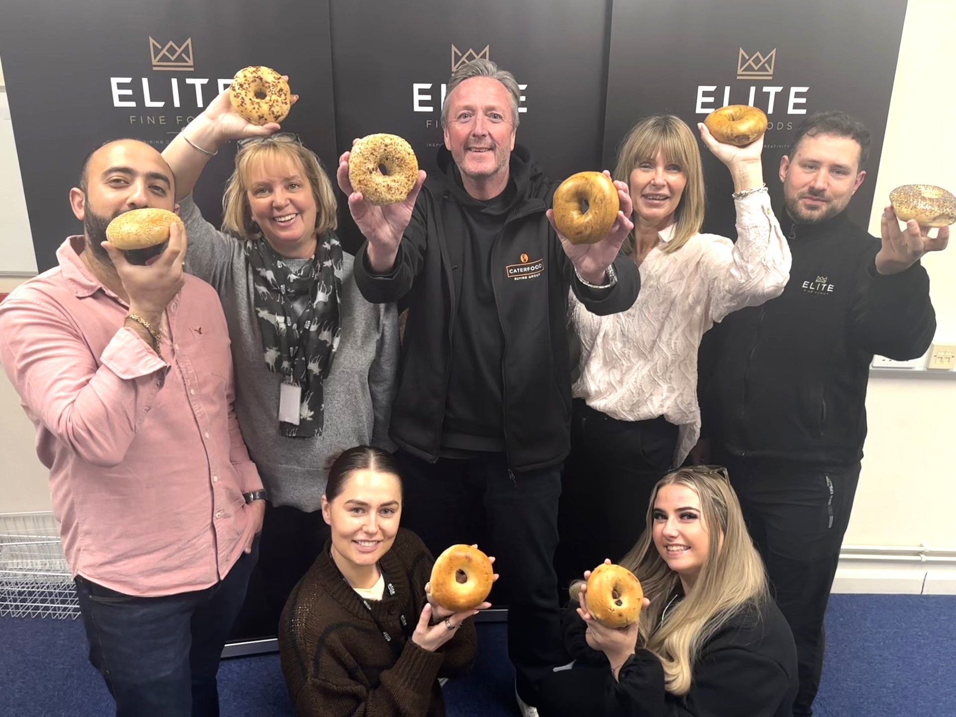 Group of seven people, smiling and holding up one of the new bagels to celebrate launching New Yorker Bagels in the UK
