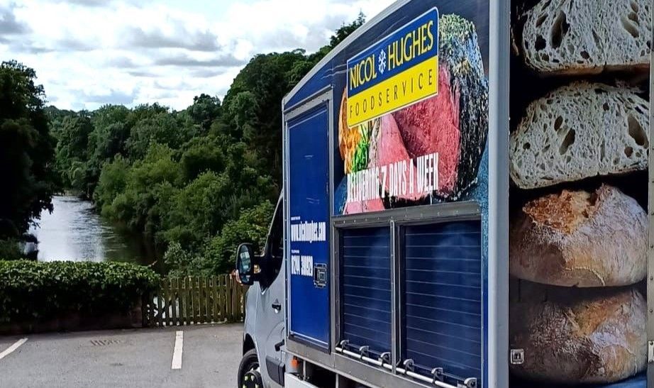 A Nicol Hughes branded delivery truck parked overlooking a pretty river view