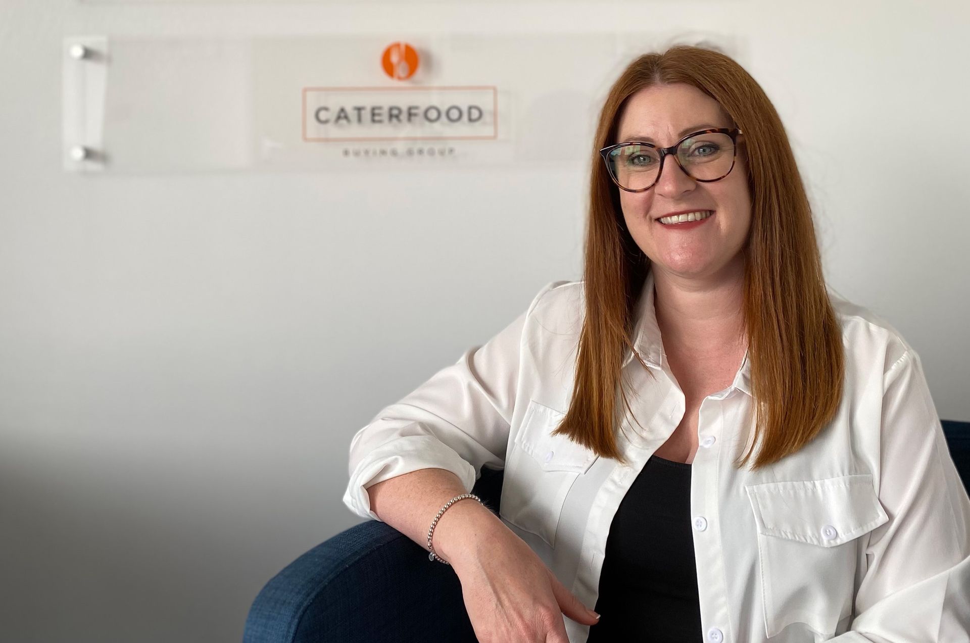 Jenny-Donnelly-Coles, Telesales Executive who has worked at South Lincs Foodservice for twenty years, smiling and sitting in a chair in the reception area of the workplace