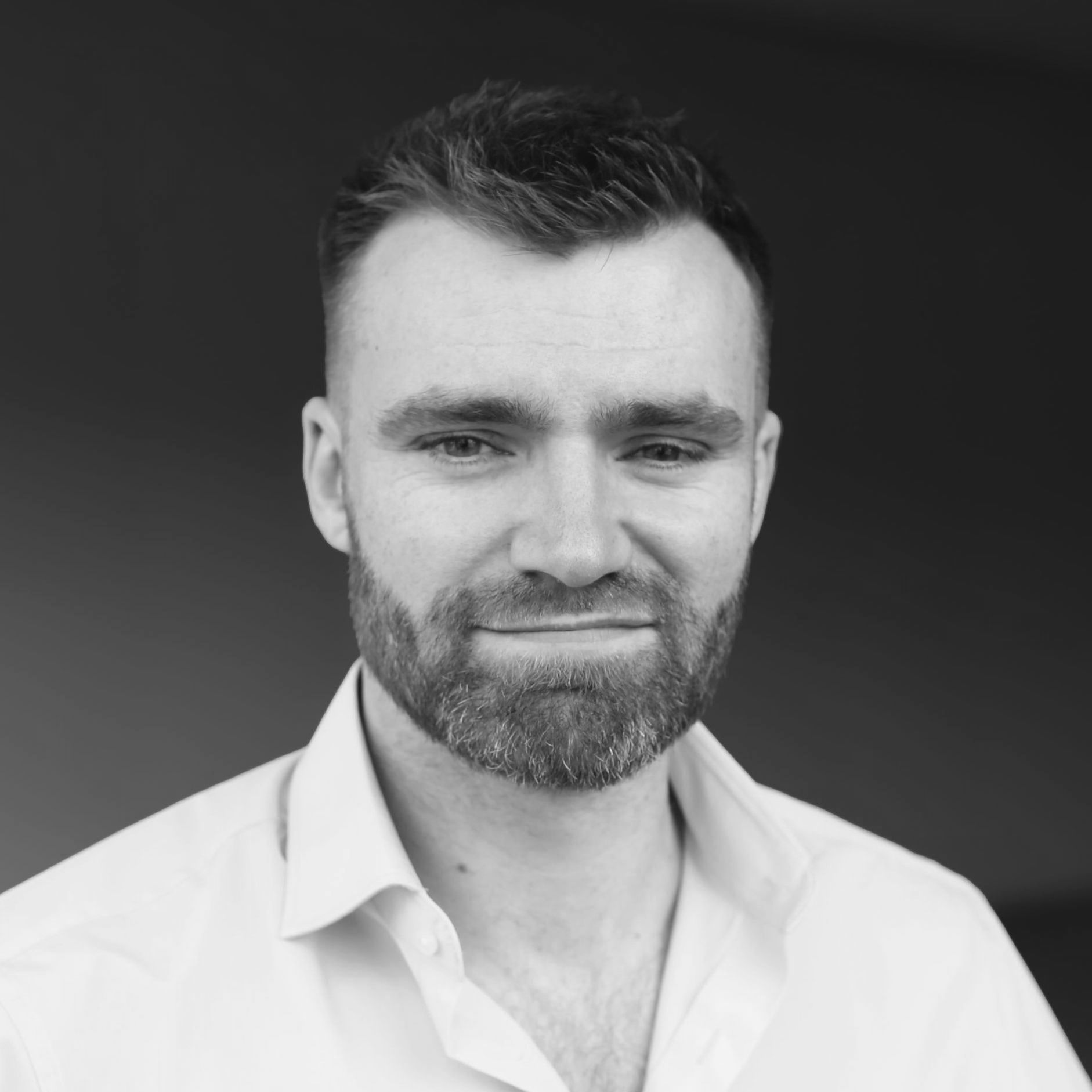 A black and white photo of a man with a beard wearing a white shirt.