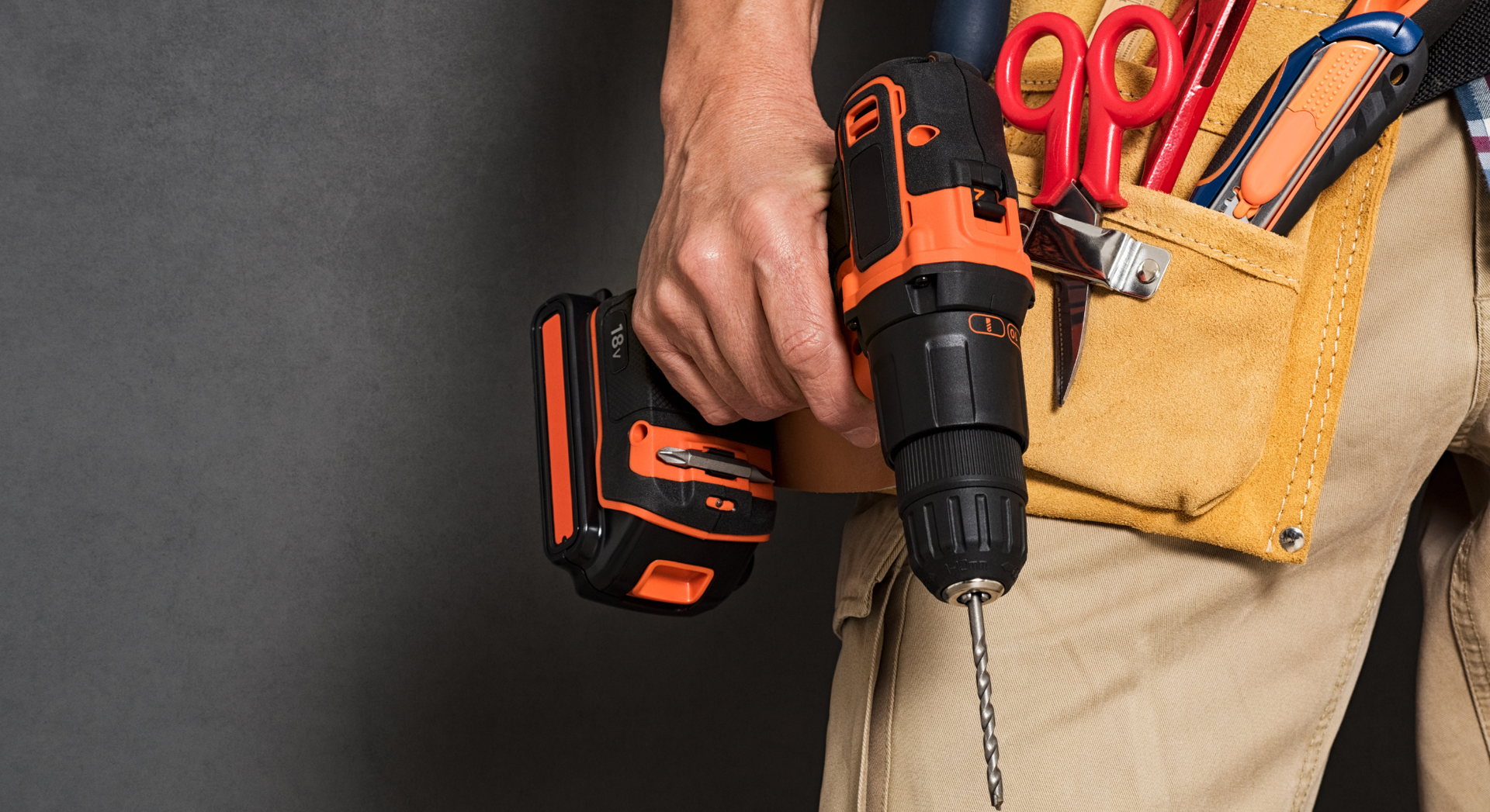 Person holding a cordless drill, wearing a tool belt with scissors.