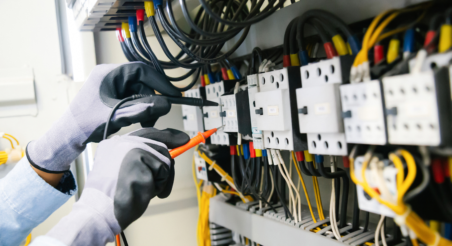 Electrician testing wires in electrical panel. Wires are yellow, blue and red.