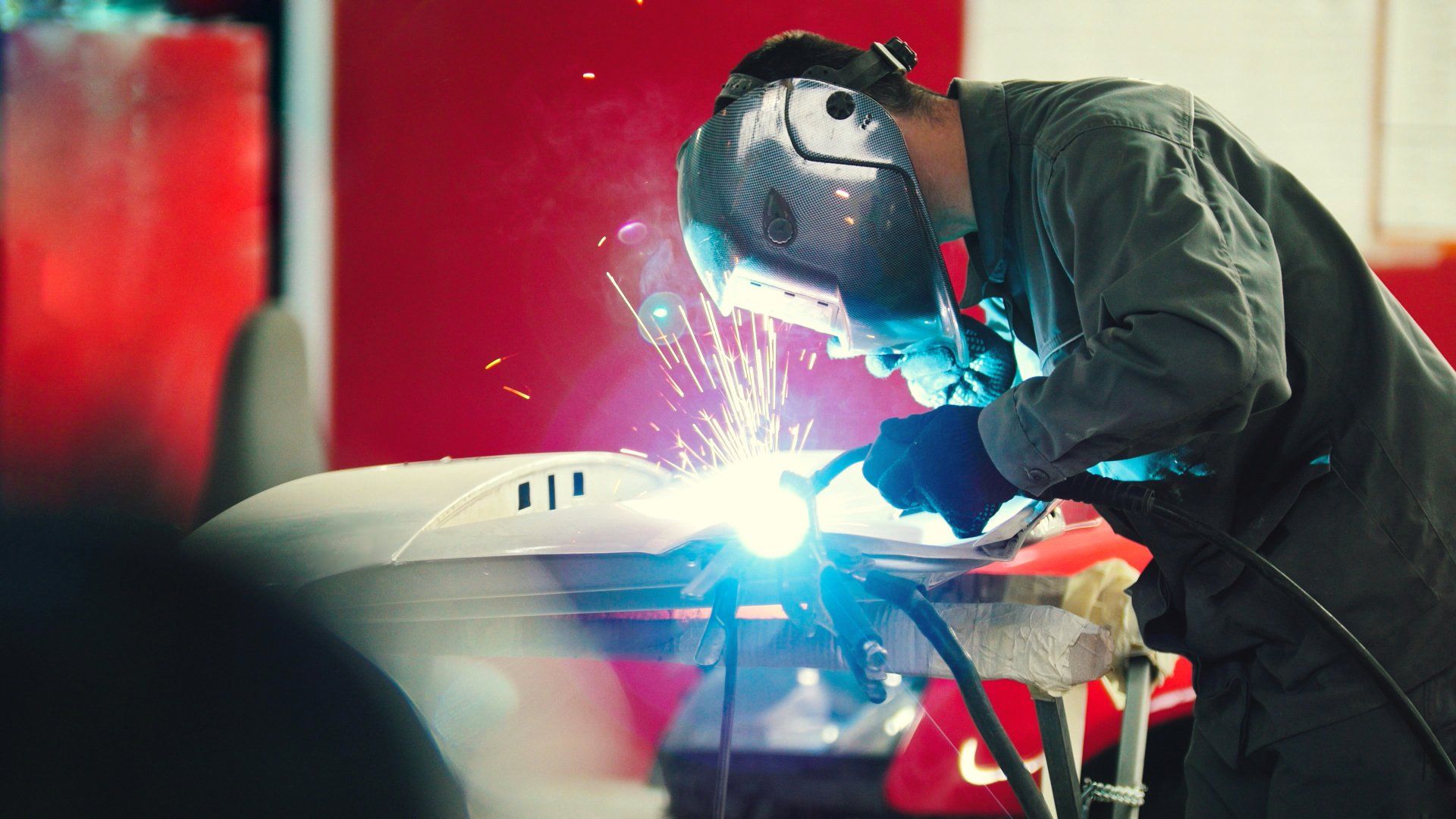 Welding industrial: worker in helmet repair detail in car auto service - blue sparklers