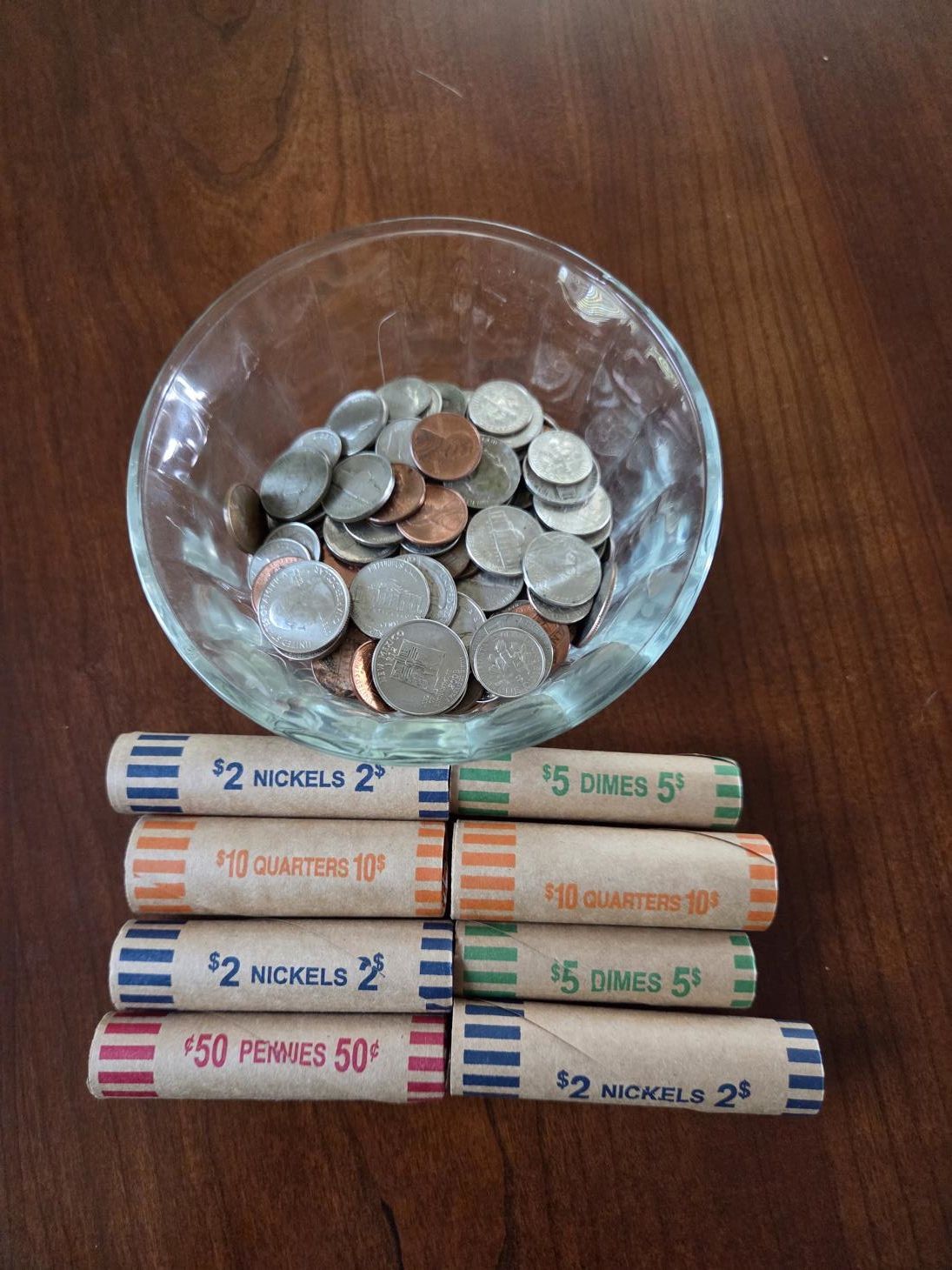 A bowl of loose change with rolls of coins on a wooden table.
