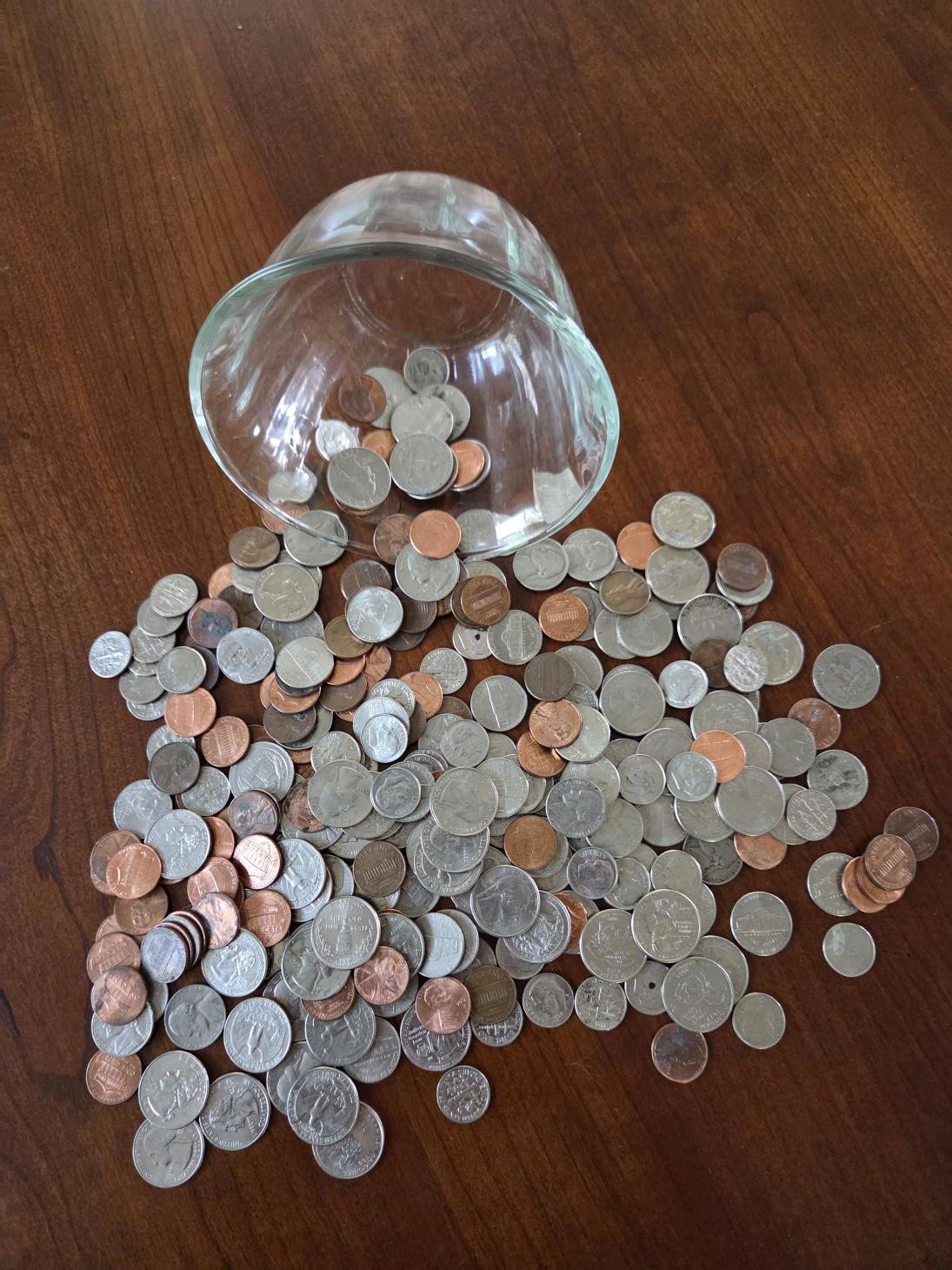 A spilled glass bowl with scattered coins on a brown wooden surface.