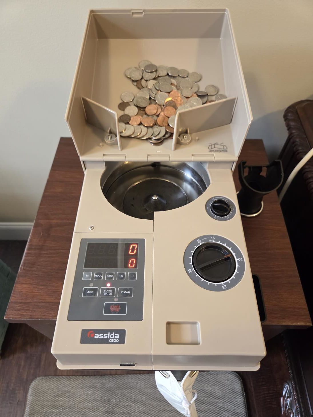Coin counter with beige exterior, counting coins on a wooden table.
