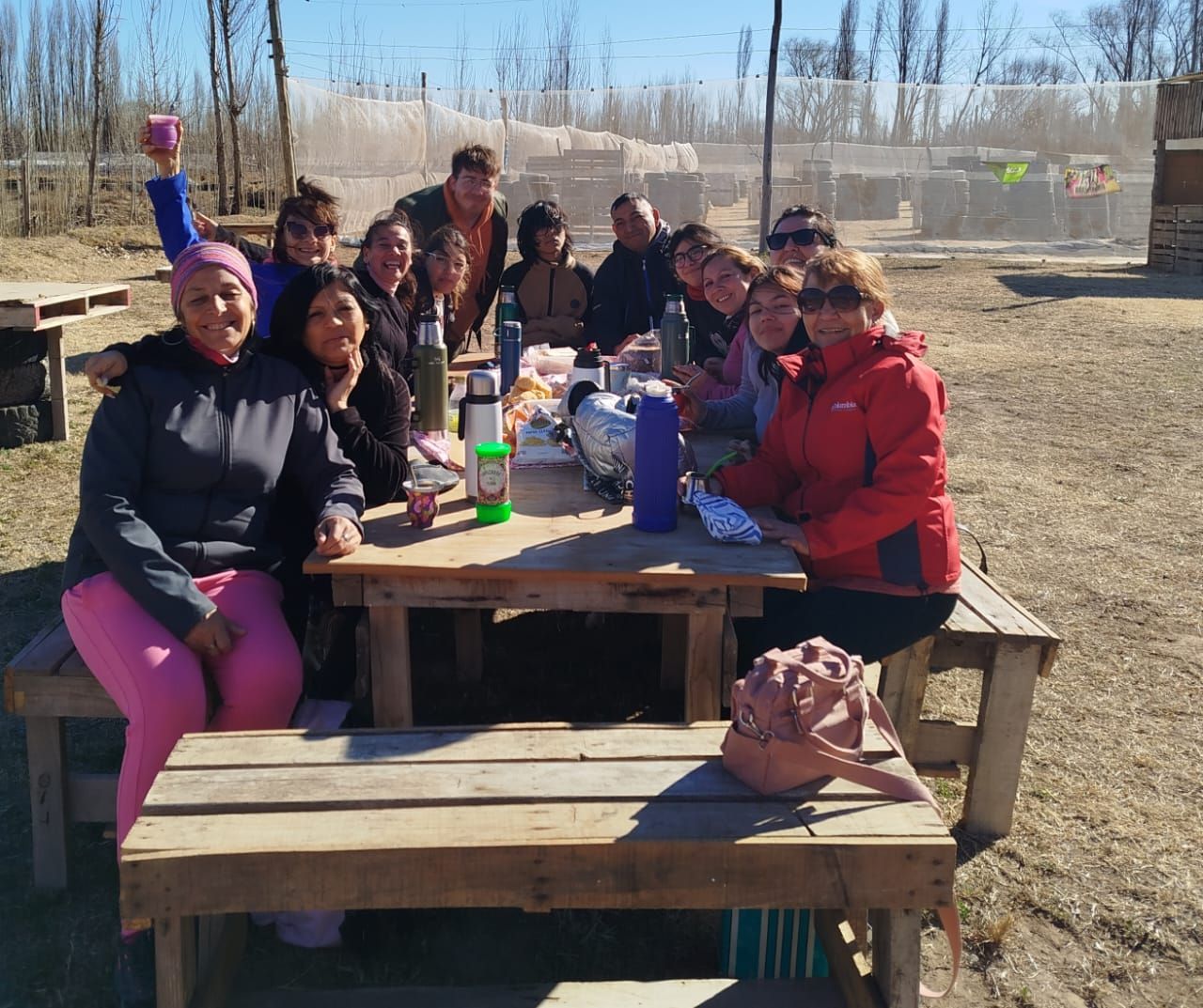Grupo de personas sonriendo alrededor de una mesa de picnic al aire libre en un día soleado.