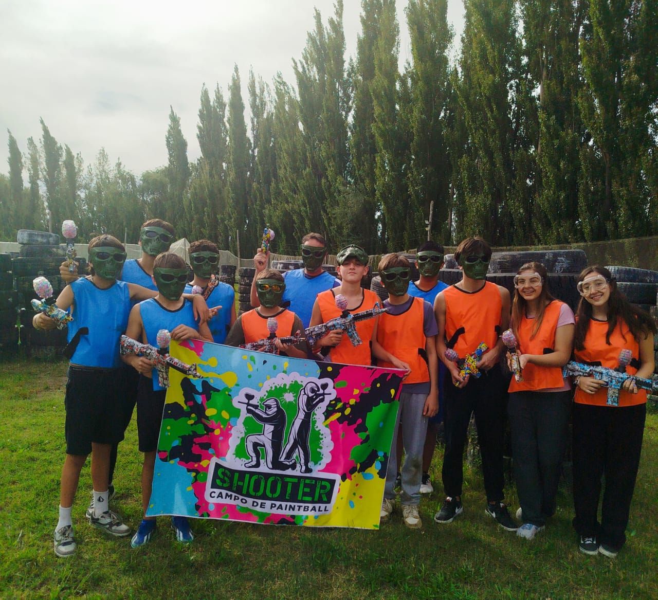 Grupo de personas con equipo de paintball posando con una pancarta de 