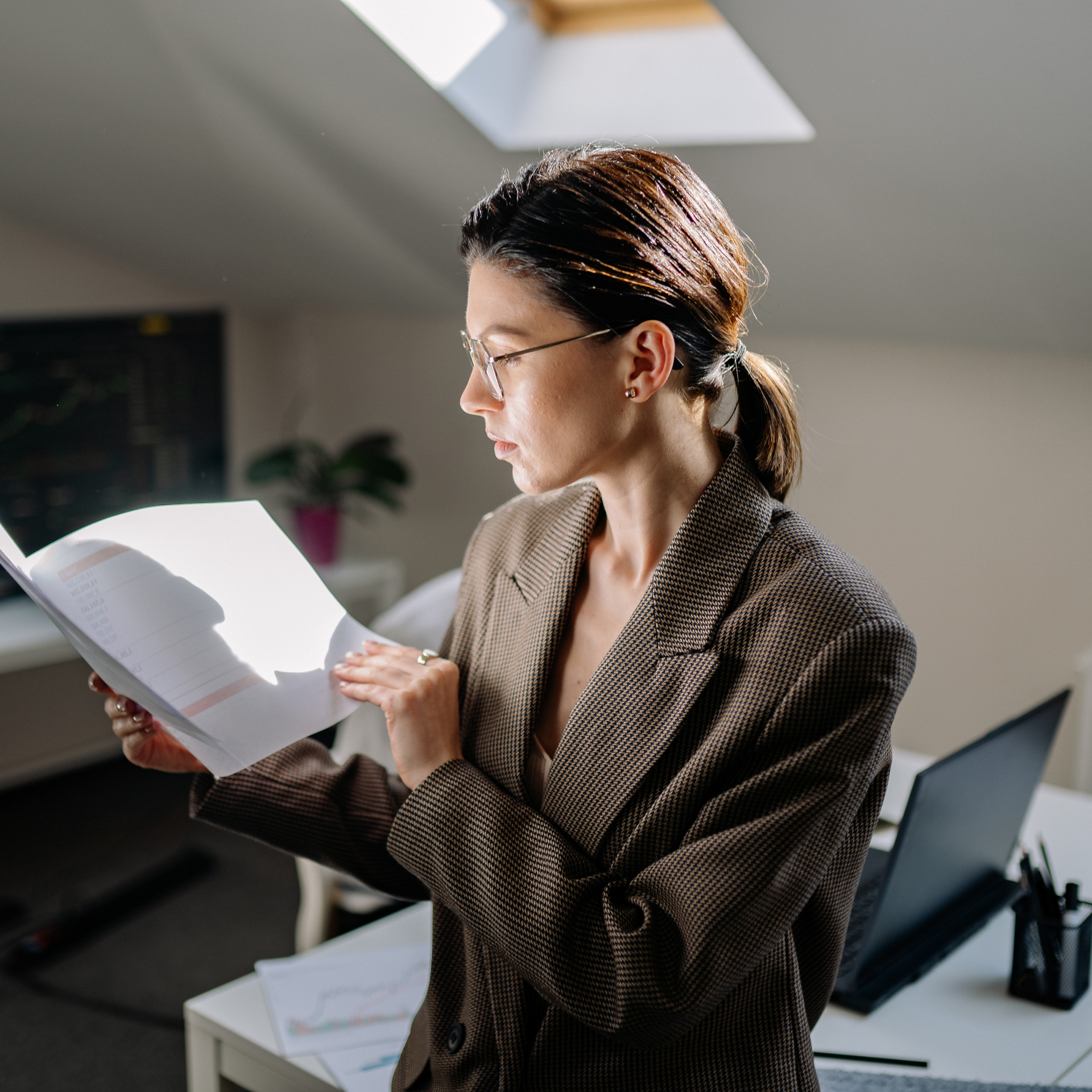 Man in suit points to papers, talking to another man at a wooden table; calculator and magnifying glass present.