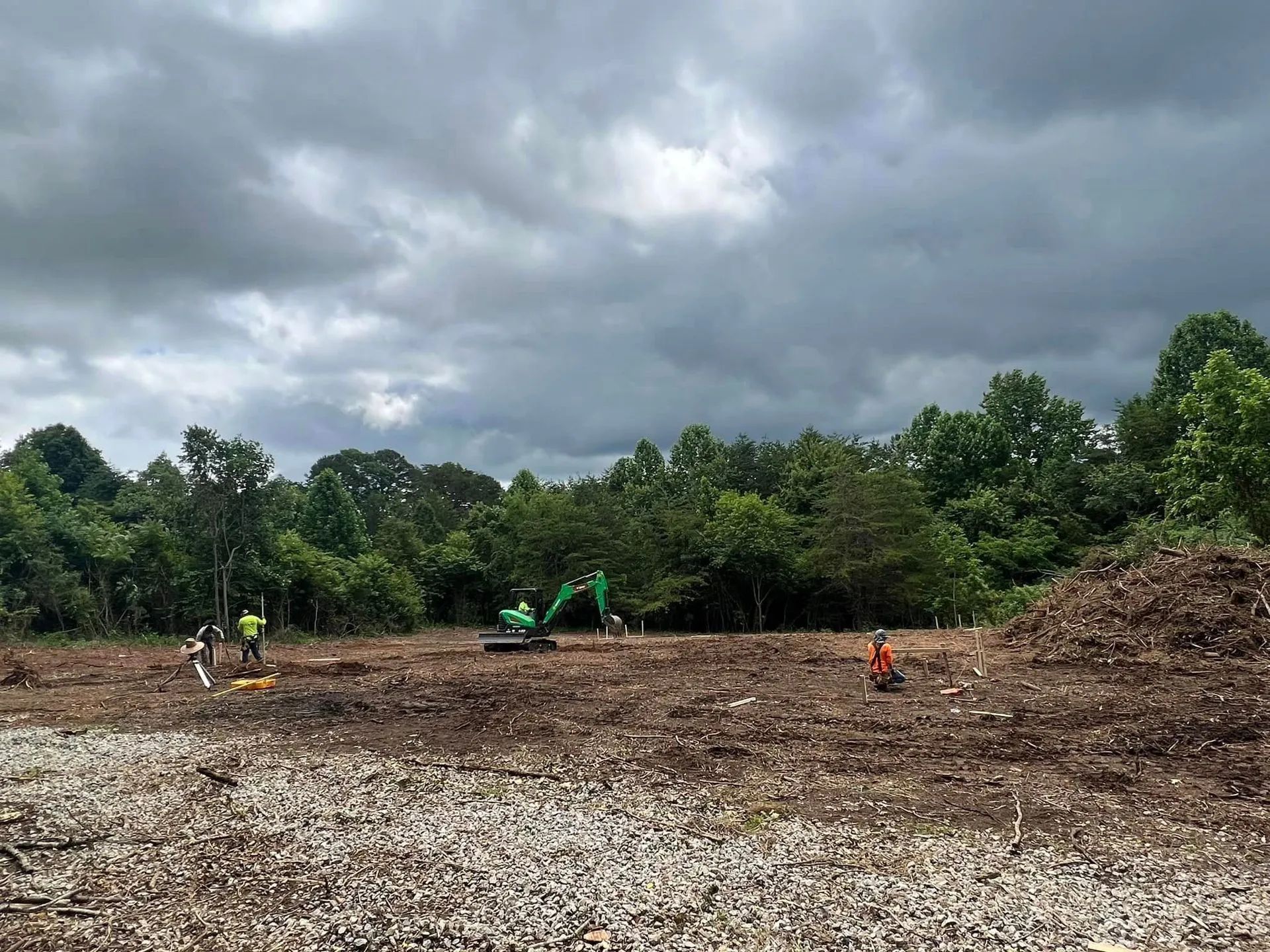 Construction site, cloudy sky. Excavator and workers clearing land near a forest.