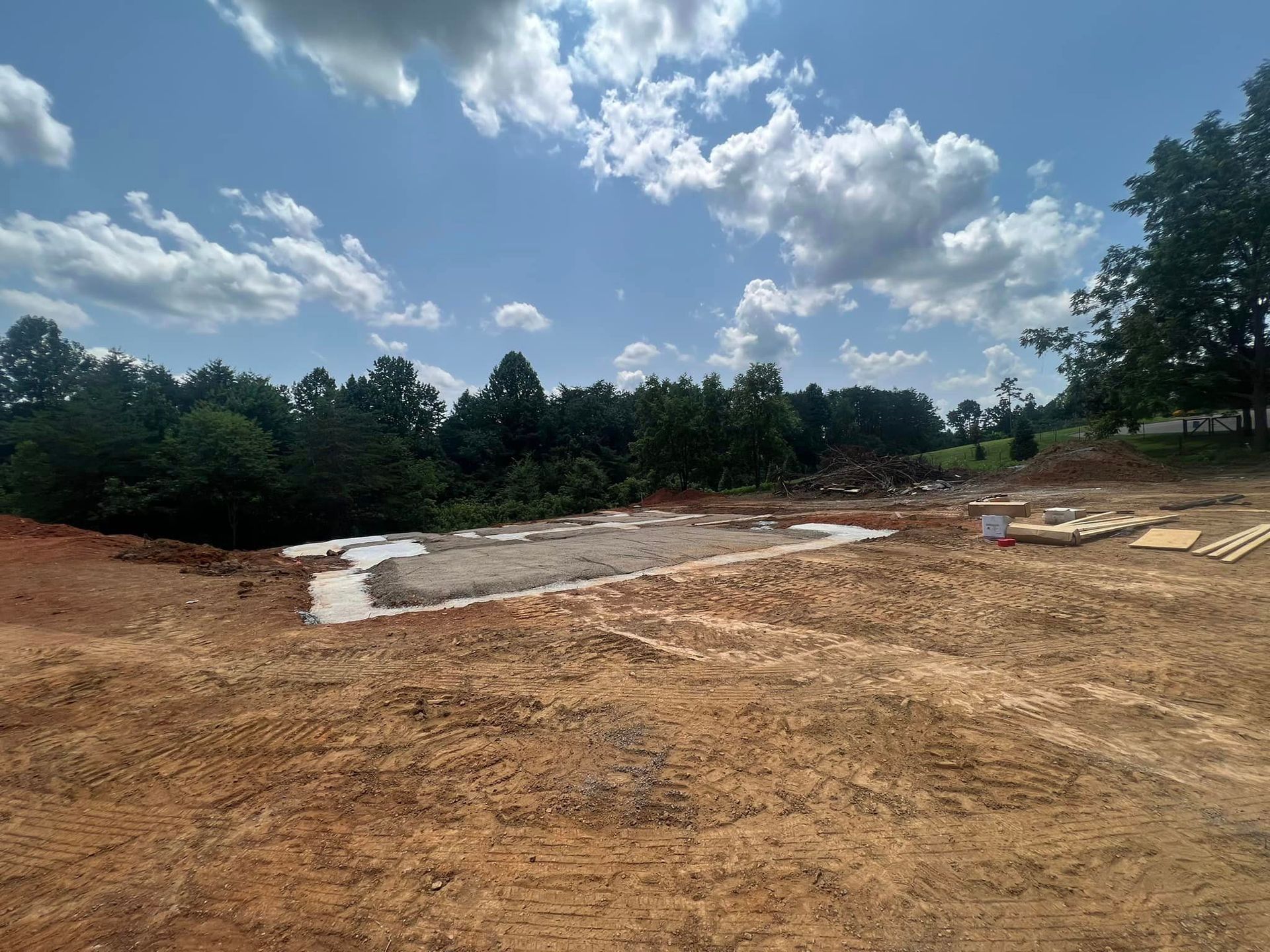 A large dirt field with trees in the background and a blue sky with clouds.
