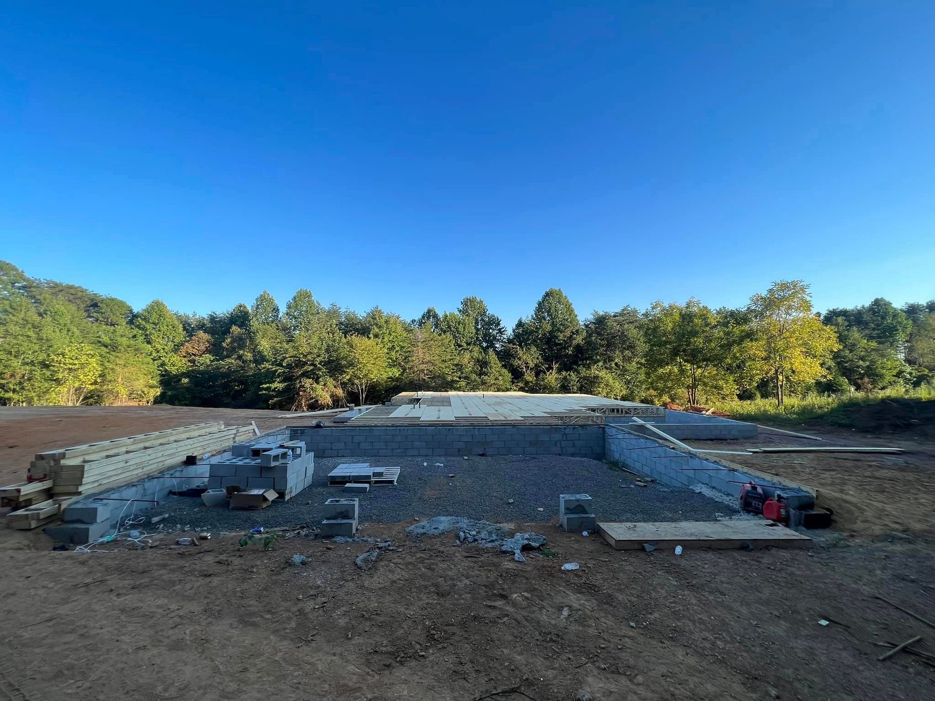 A large swimming pool is being built in a dirt field with trees in the background.