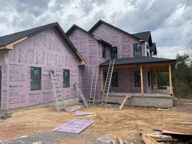 A large house is being built with purple insulation and a porch.