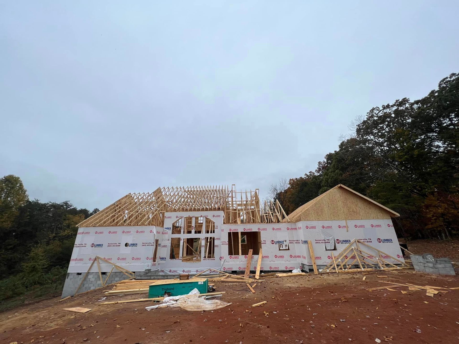 A house is being built on top of a dirt hill surrounded by trees.