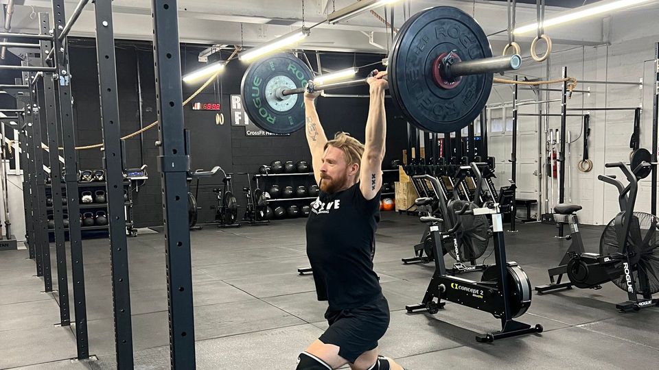 a man lifting a barbell in a gym with a rogue logo on the wall