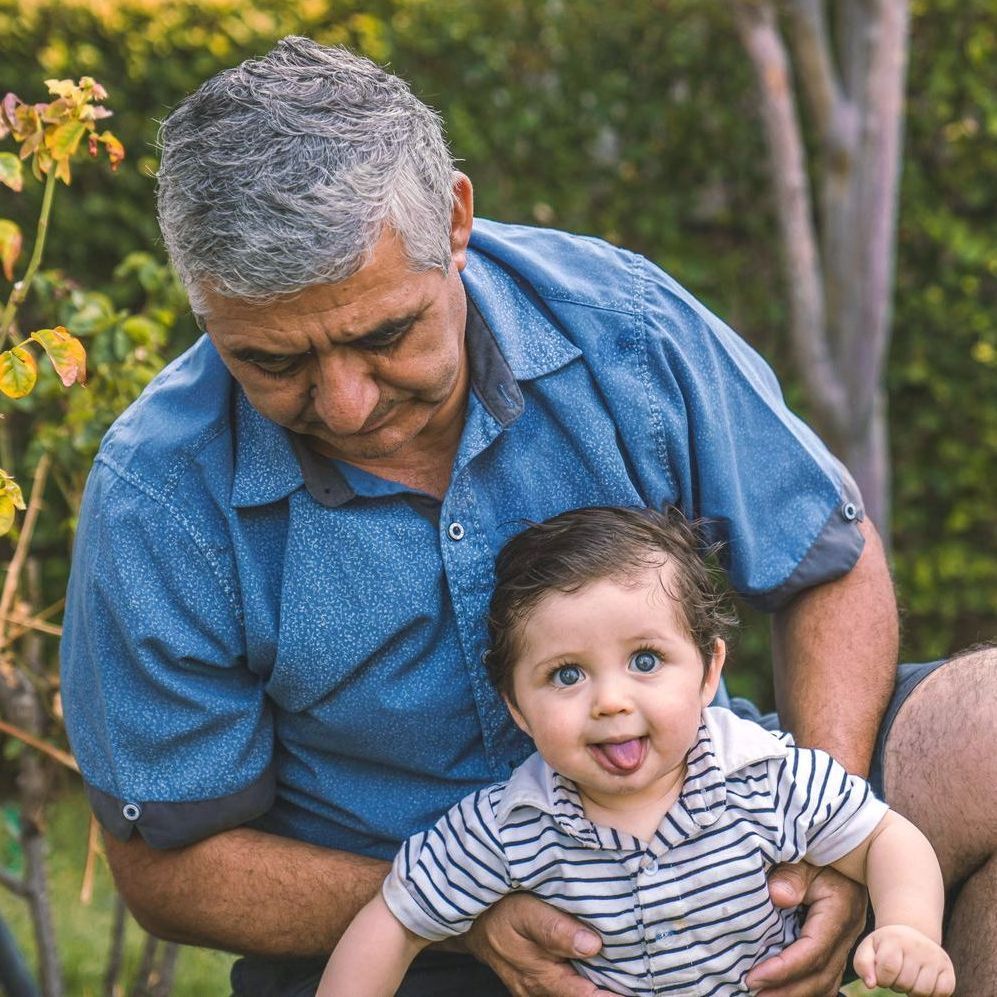 A man is holding a baby in his arms and the baby is sticking out his tongue.