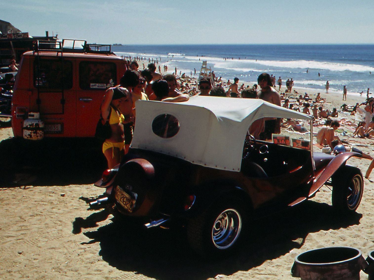 A red van is parked on the beach next to a vintage buggy