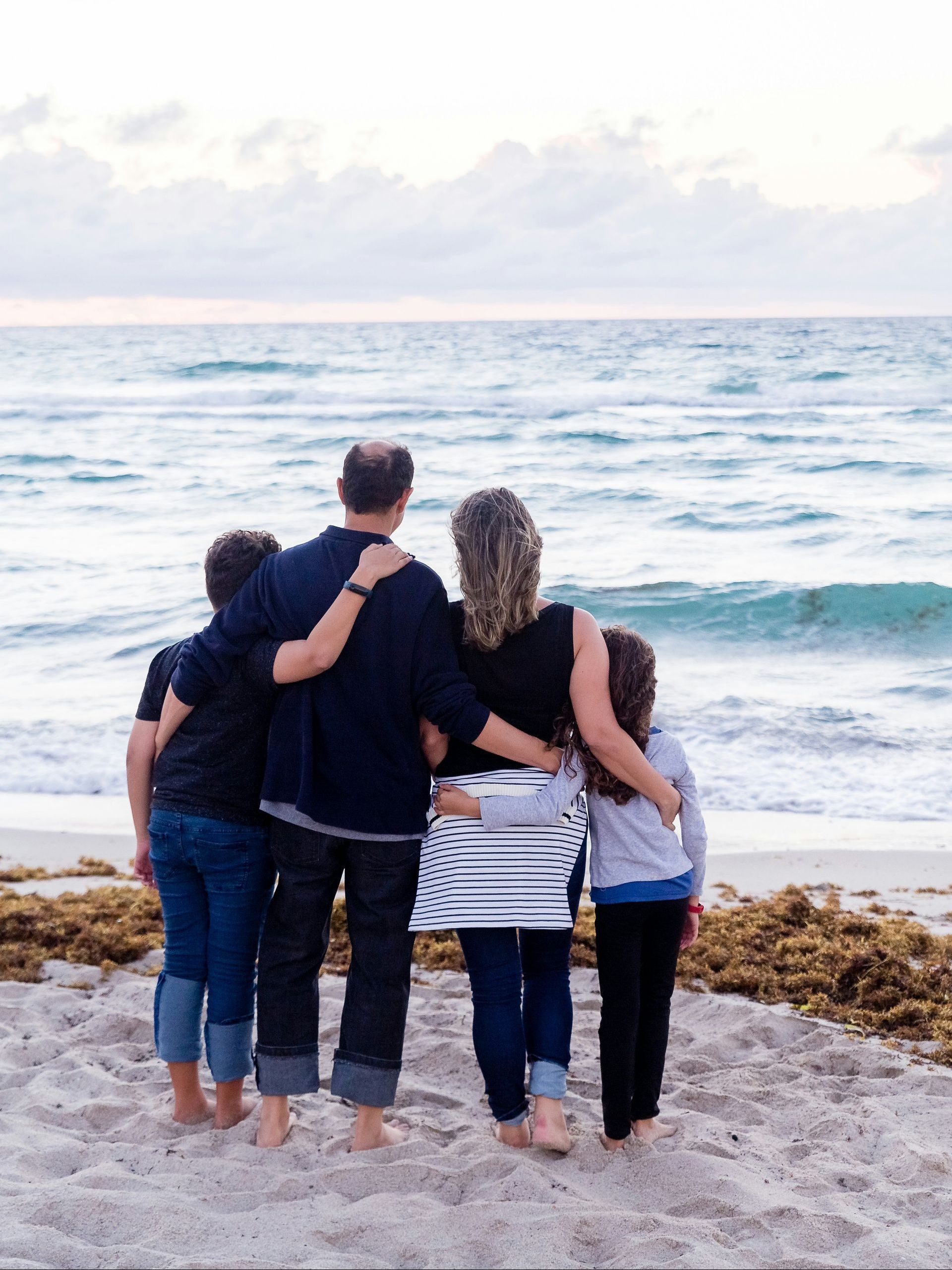 A family is standing on the beach looking at the ocean.