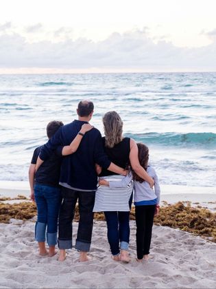 A family is standing on the beach looking at the ocean.