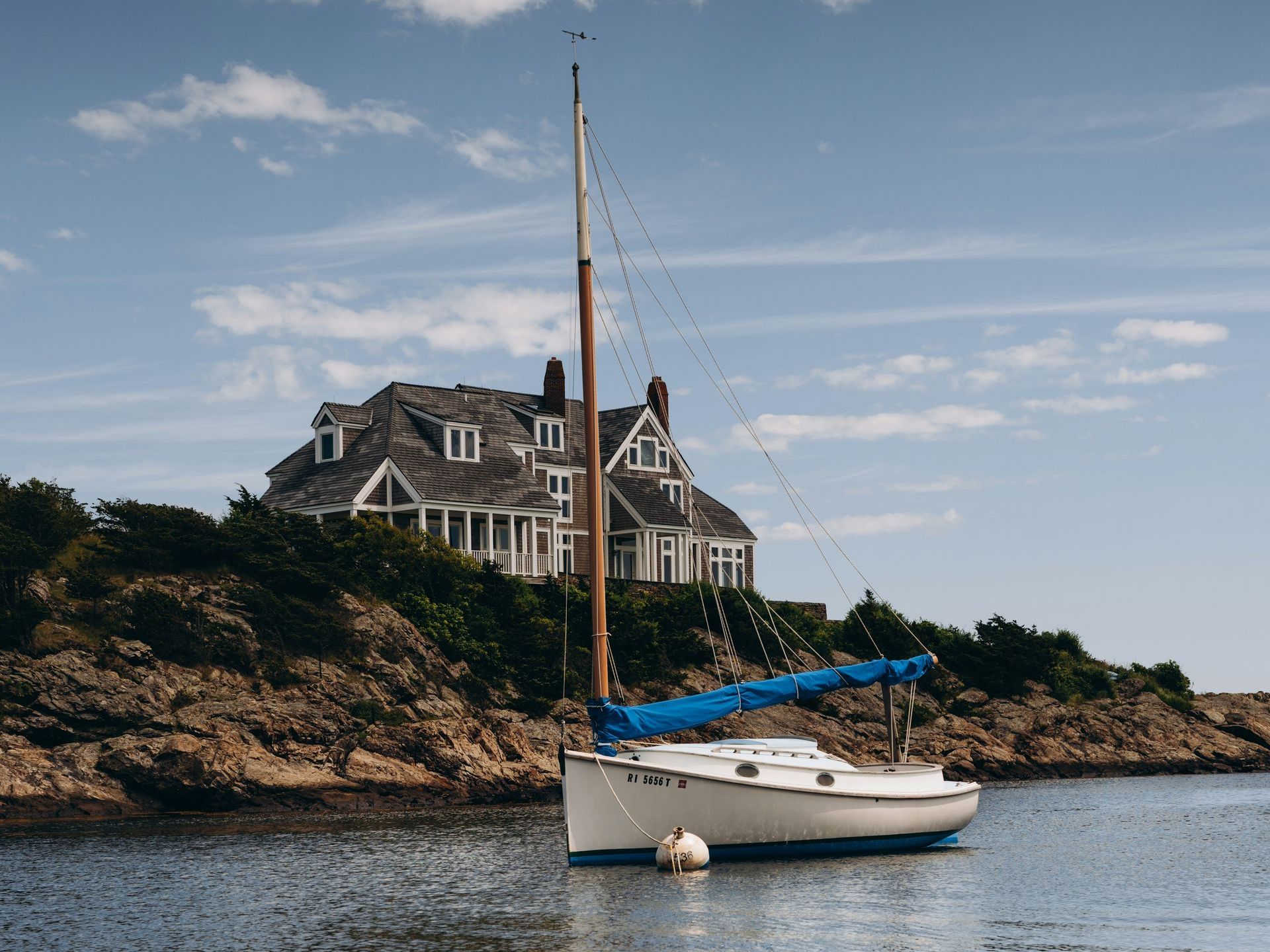 A sailboat is docked in the water with a house in the background.