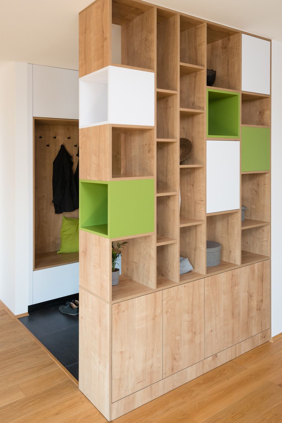 Wooden room divider with open shelving, some white and green blocks, next to a coat closet.