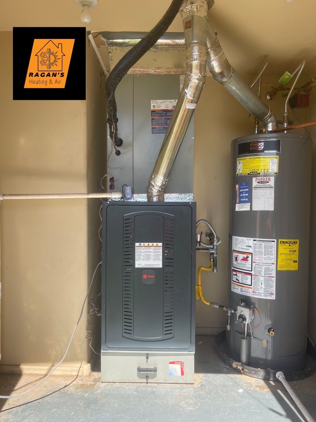 Furnace and water heater in a utility room. Gray appliances, silver vent pipes, and beige walls.