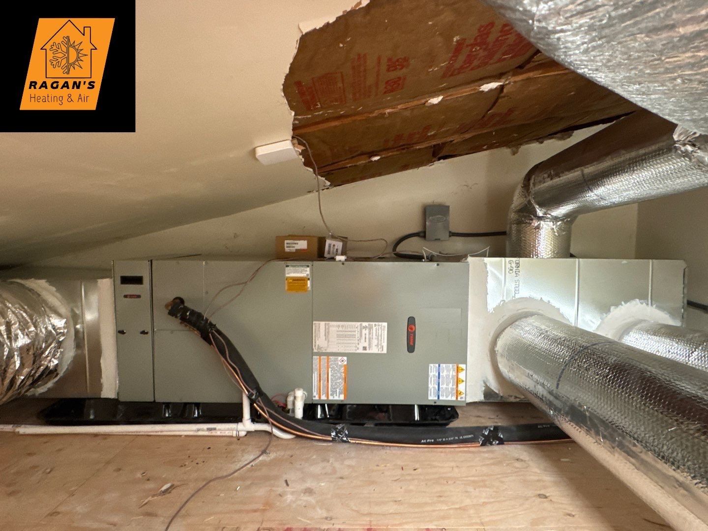HVAC unit installed in an attic space. Metal ducts with insulation, electrical wiring, and exposed wood.