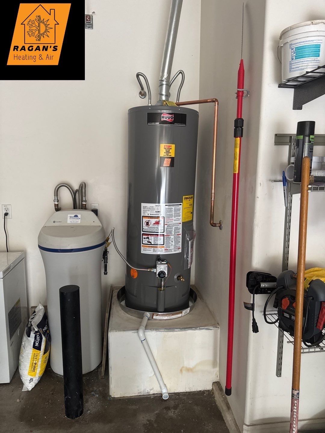 A water heater in a garage next to a water softener and storage.