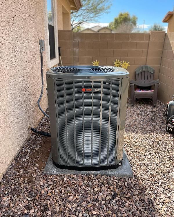 A large air conditioner is sitting on top of a pile of gravel outside of a house.