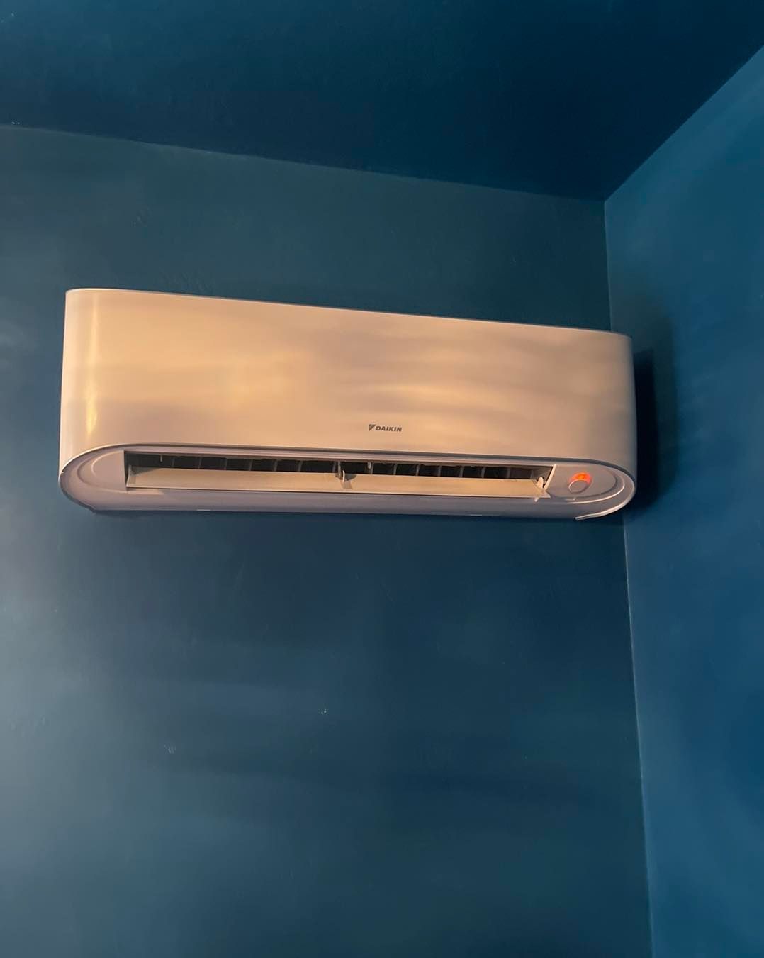 A white air conditioner is hanging on a blue wall.