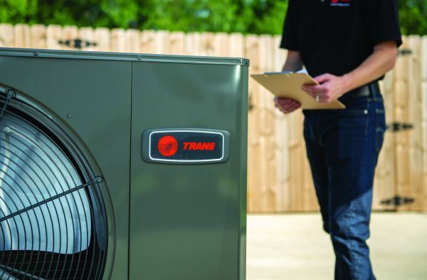 A man is standing in front of a trane air conditioner