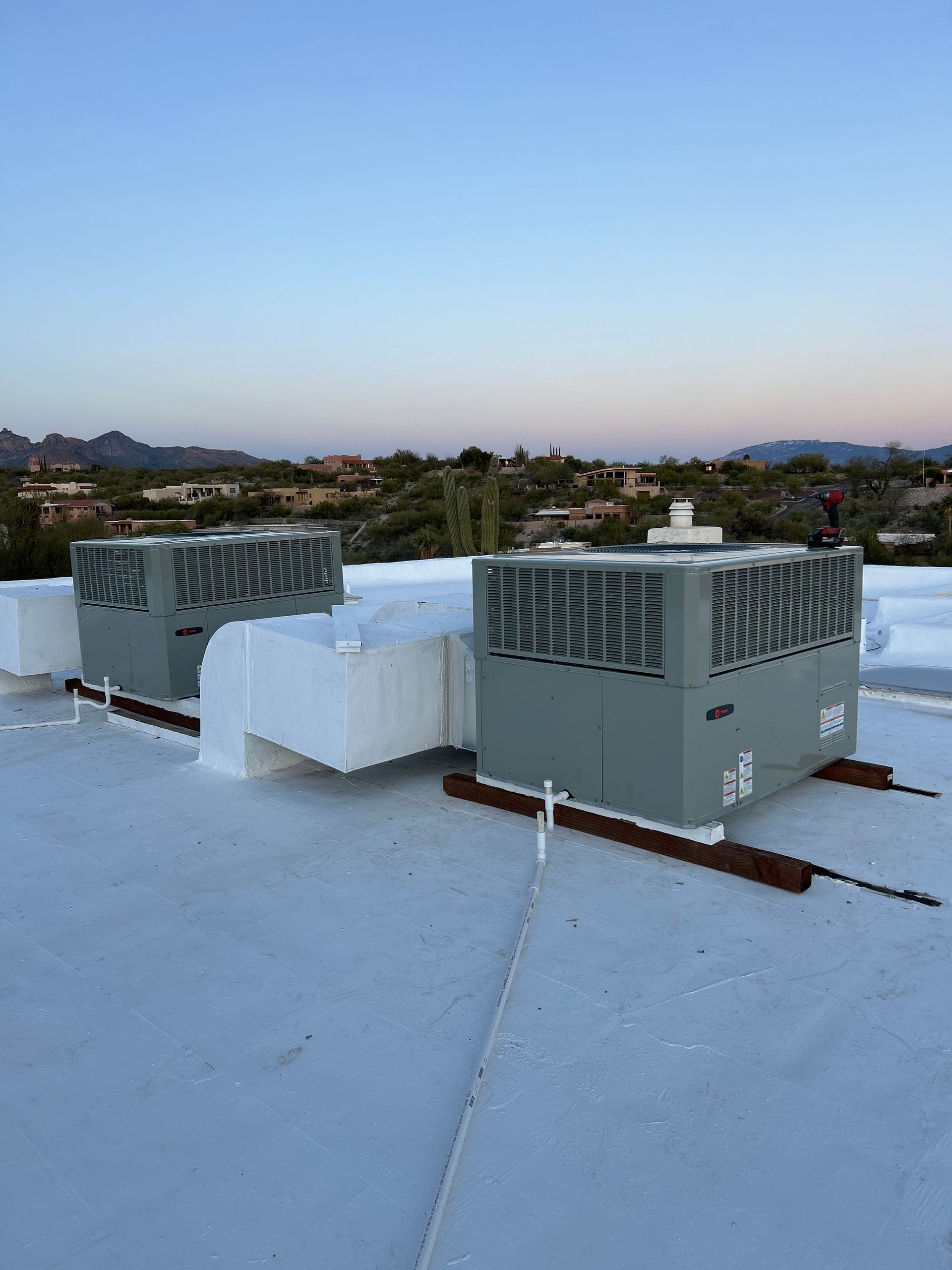 HVAC units on a white flat roof against a mountain backdrop under a blue sky.