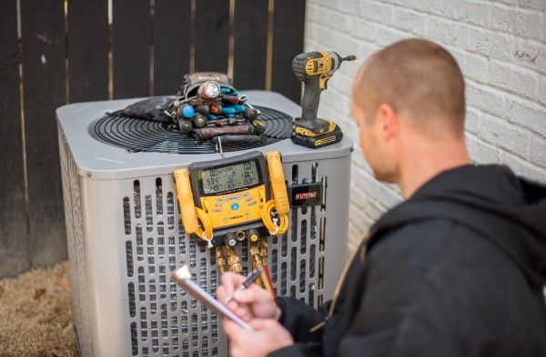 A man is working on an air conditioner while holding a clipboard.