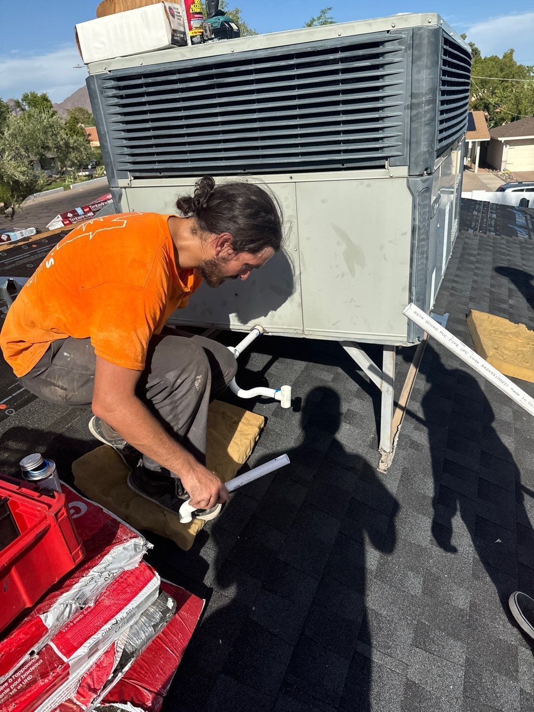 A man is working on an air conditioner on top of a roof.