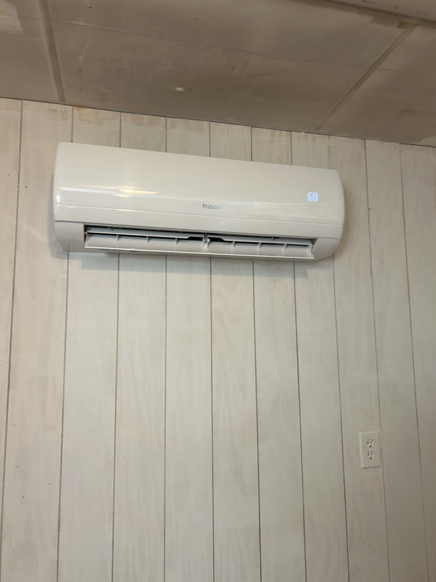 A white air conditioner is hanging on a white wooden wall.