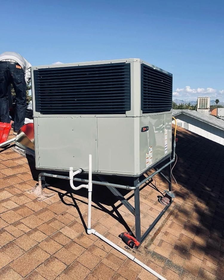 A man is standing on top of a roof next to a large air conditioner.