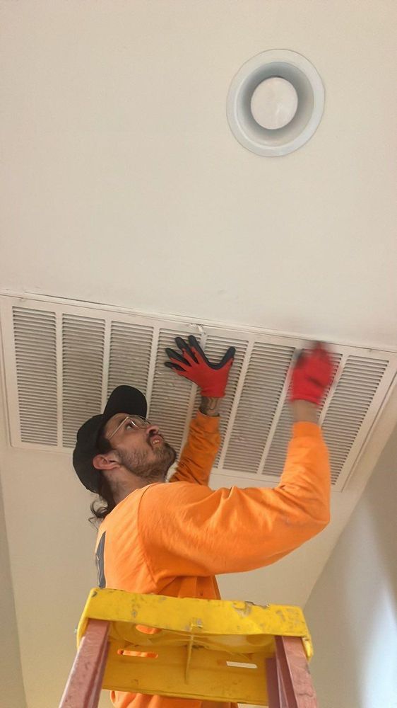 A man is standing on a ladder fixing an air vent on the ceiling.