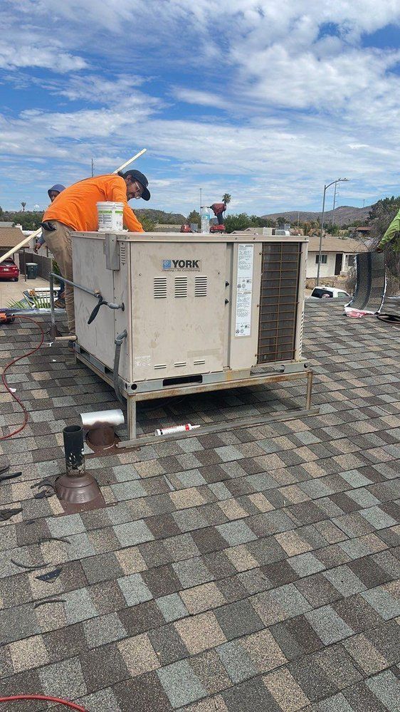 A man is working on an air conditioner on top of a roof.