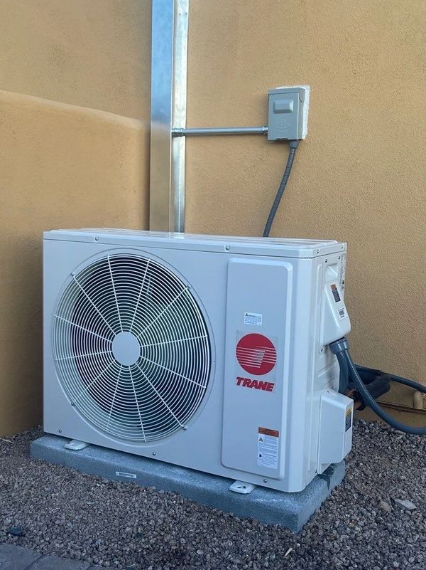 A white air conditioner is sitting on the ground next to a wall.