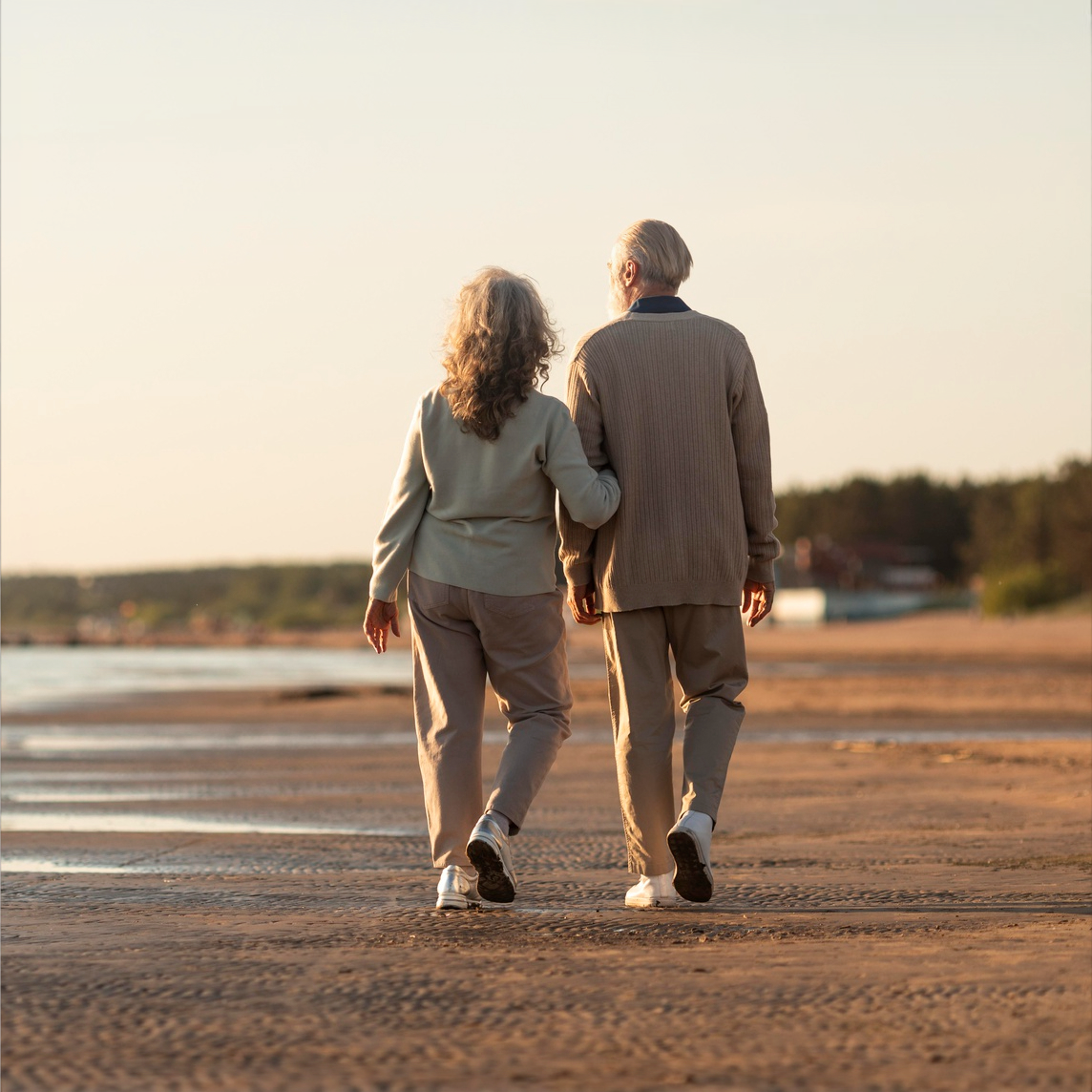 A man and a woman are walking on the beach holding hands.