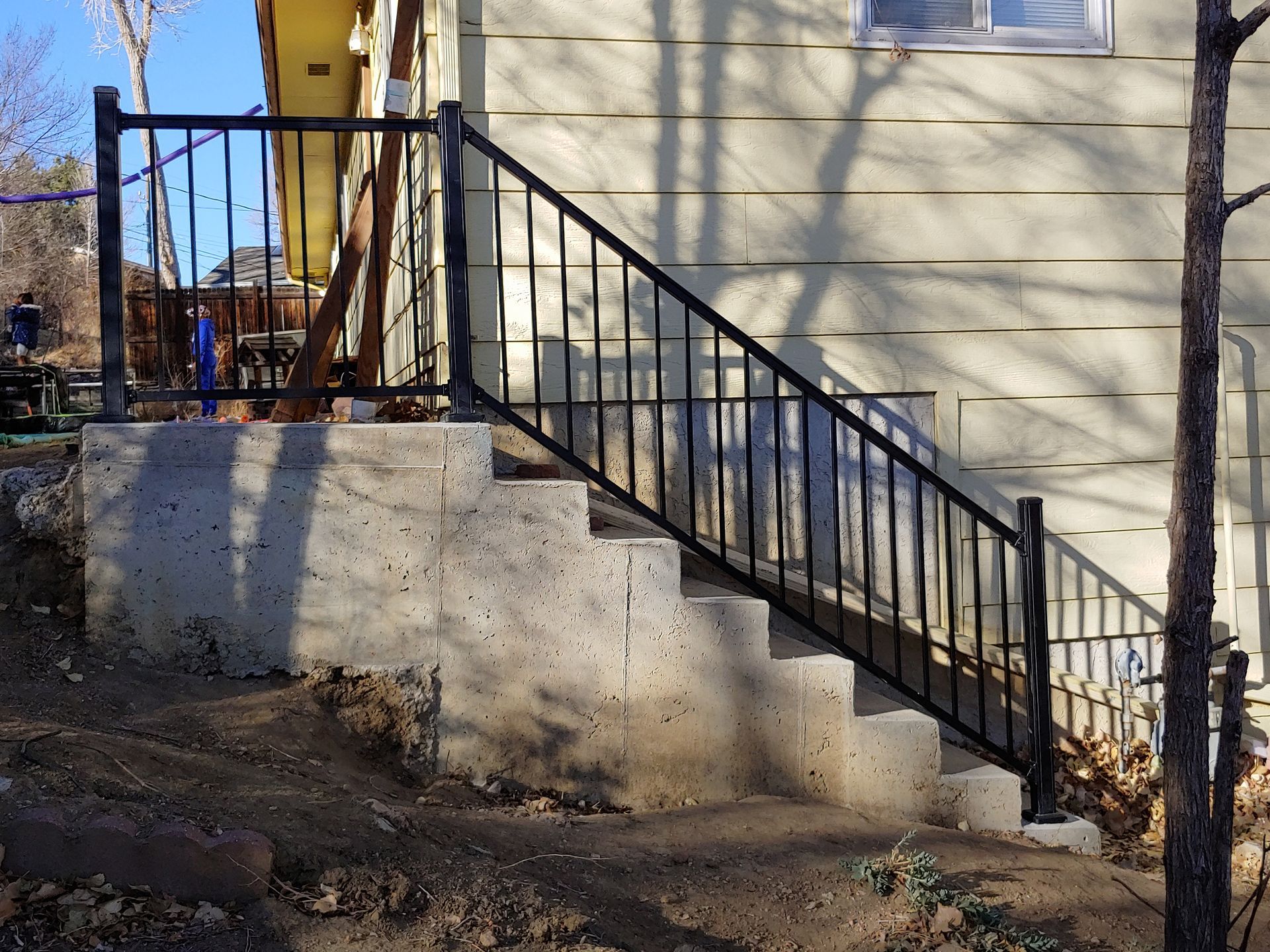 Concrete steps with black metal railing leading up to a beige house exterior.