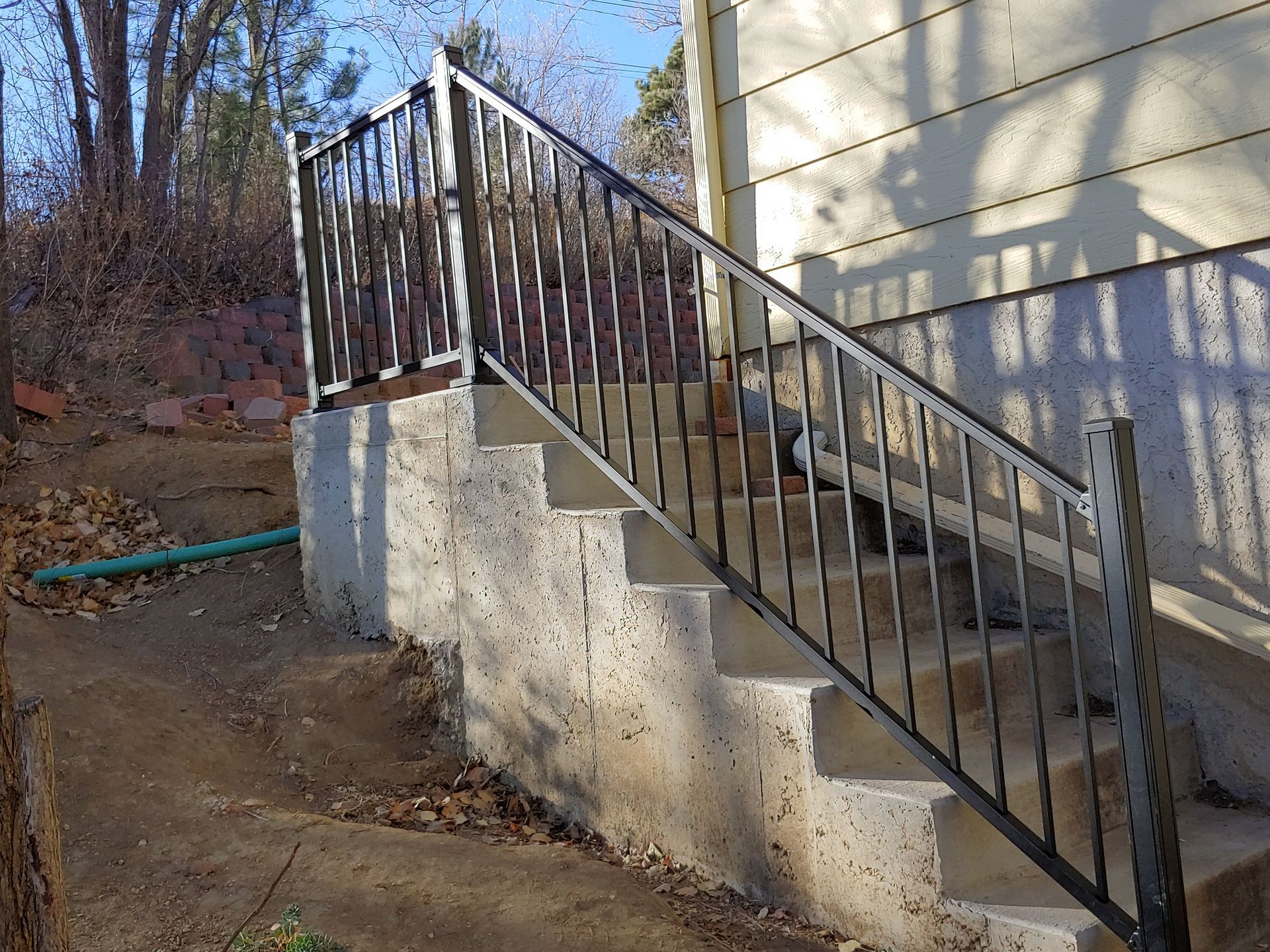 Concrete stairs with black metal handrails leading up to a light-colored building.