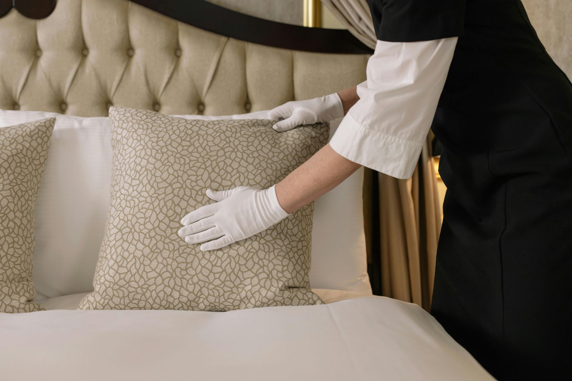 Person in uniform and gloves making a bed, arranging a patterned pillow.